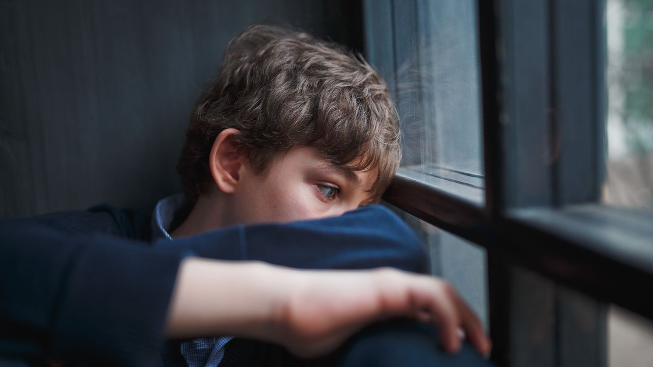 Einsamer Junge sitzt traurig am Fenster und verbirgt Gesicht
