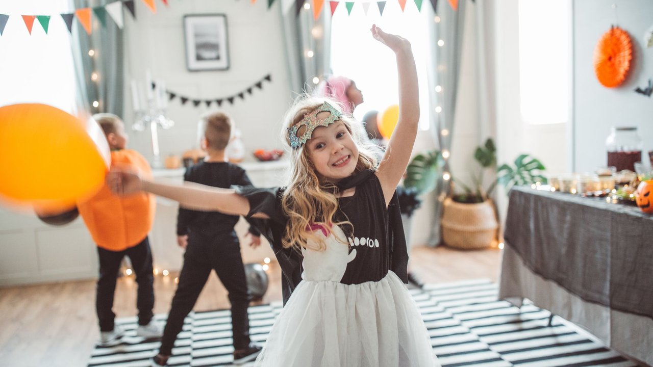 Multi ethnic group of children have party at home, they wear costumes, celebrating Halloween, dancing and jumping