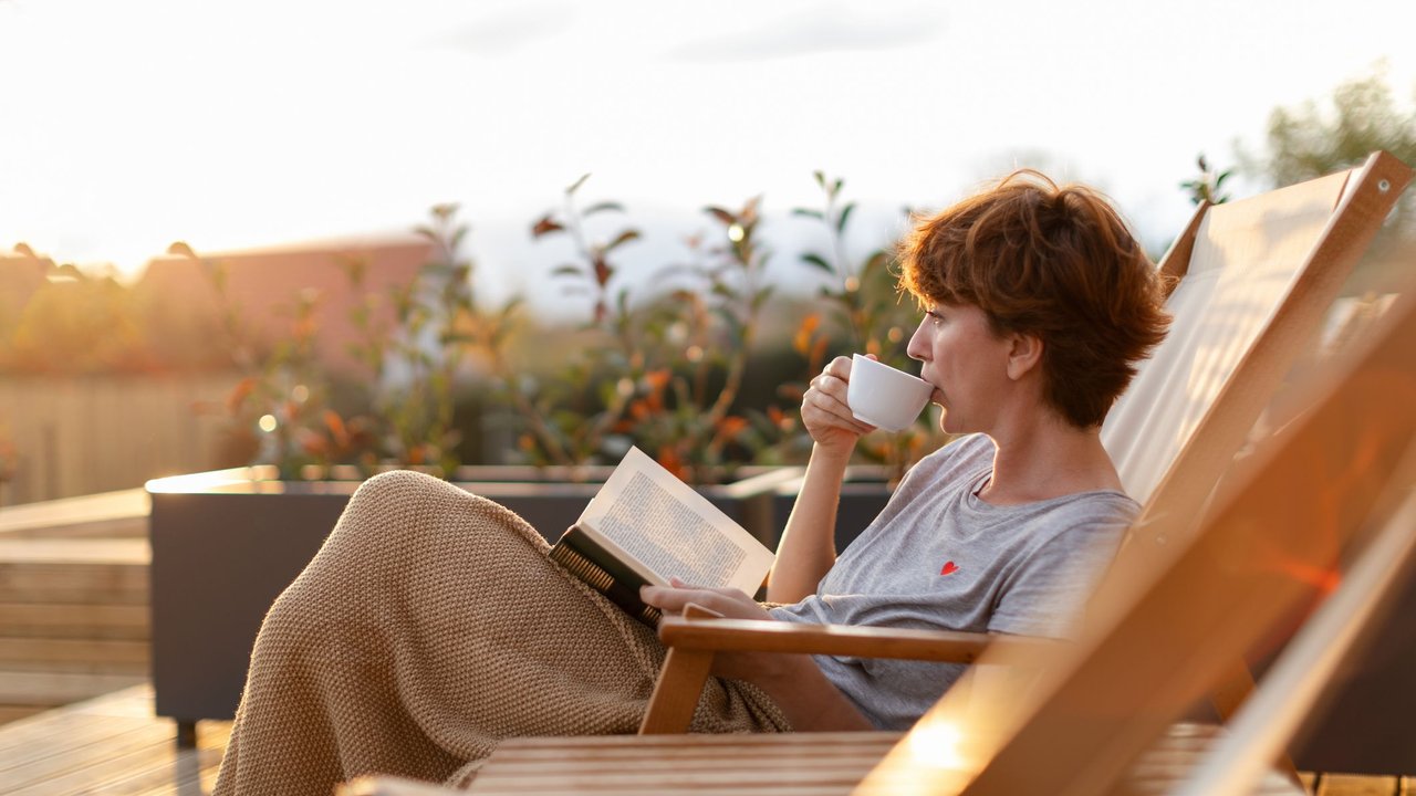 Frau sitzt mit einem Buch auf der Terrasse und trinkt Tee