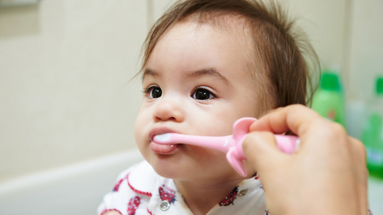 Brushing teeth of small baby girl in bathroom