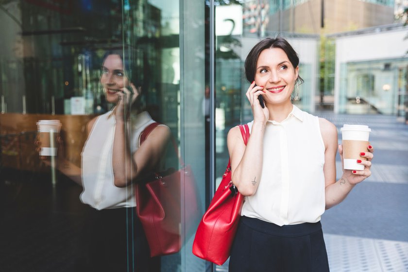 Young businesswoman with takeaway coffee reflected in glass front talking on the phone, Berlin, Germany model released Symbolfoto PUBLICATIONxINxGERxSUIxAUTxHUNxONLY WPEF02193