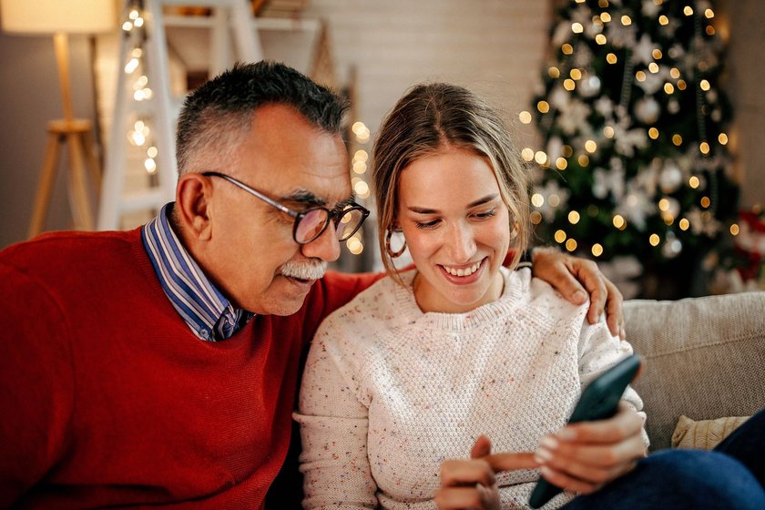 Senior men and his granddaughter spending time together in living room, using smart phone to finding the presents