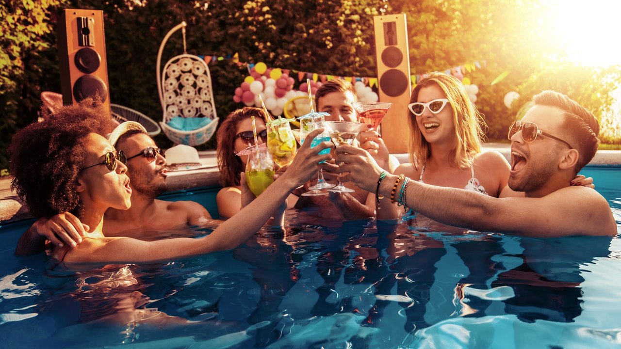 Lachende Freunde im Pool mit Cocktails
