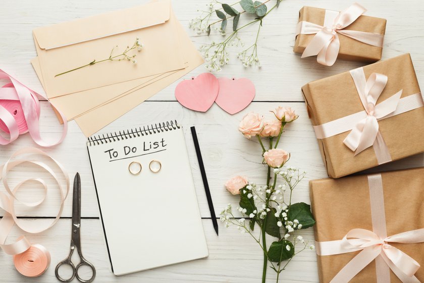 Wedding background with checklist. Paper planner and craft envelopes on white wooden table with lots of tender bridal stuff, top view