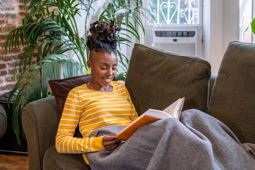 Black woman reading a book and relaxing on the couch