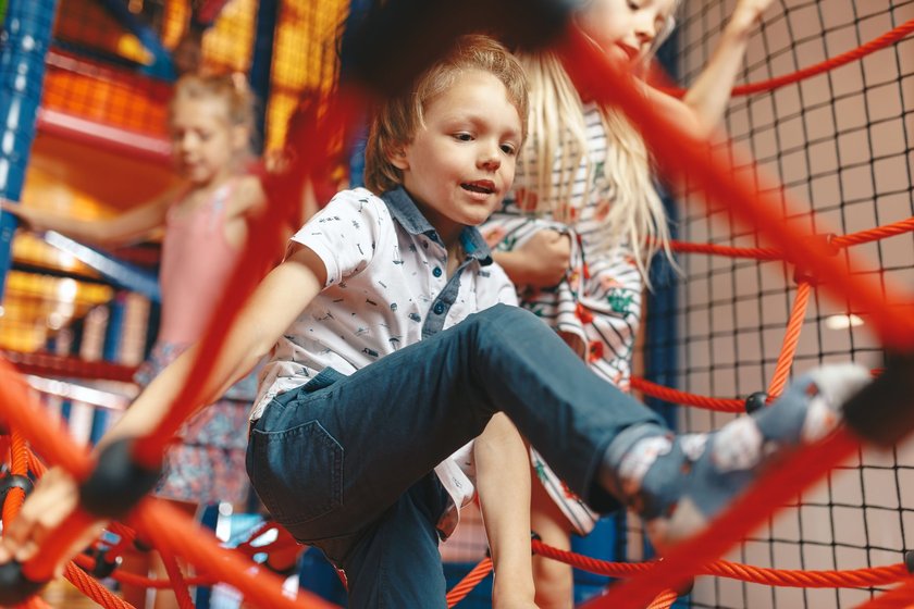 Kindergeburtstag feiern Indoorspielplatz: Junge klettert mit anderen Kindern 