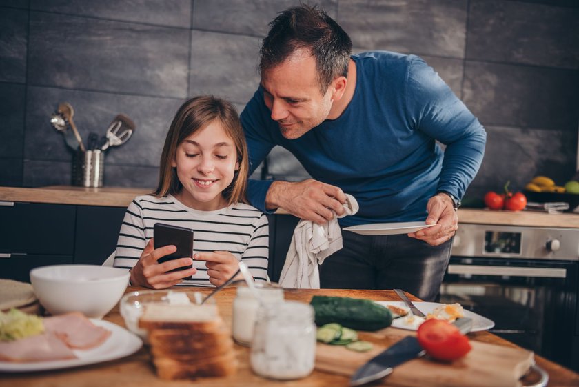 Whatsapp Guten Morgen Sprüche: Vater und Tochter beim Frühstück schauen auf Handy