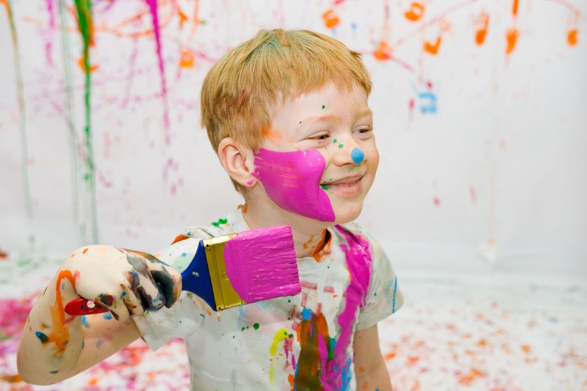 The child draws with bright paint on his face and laughs 