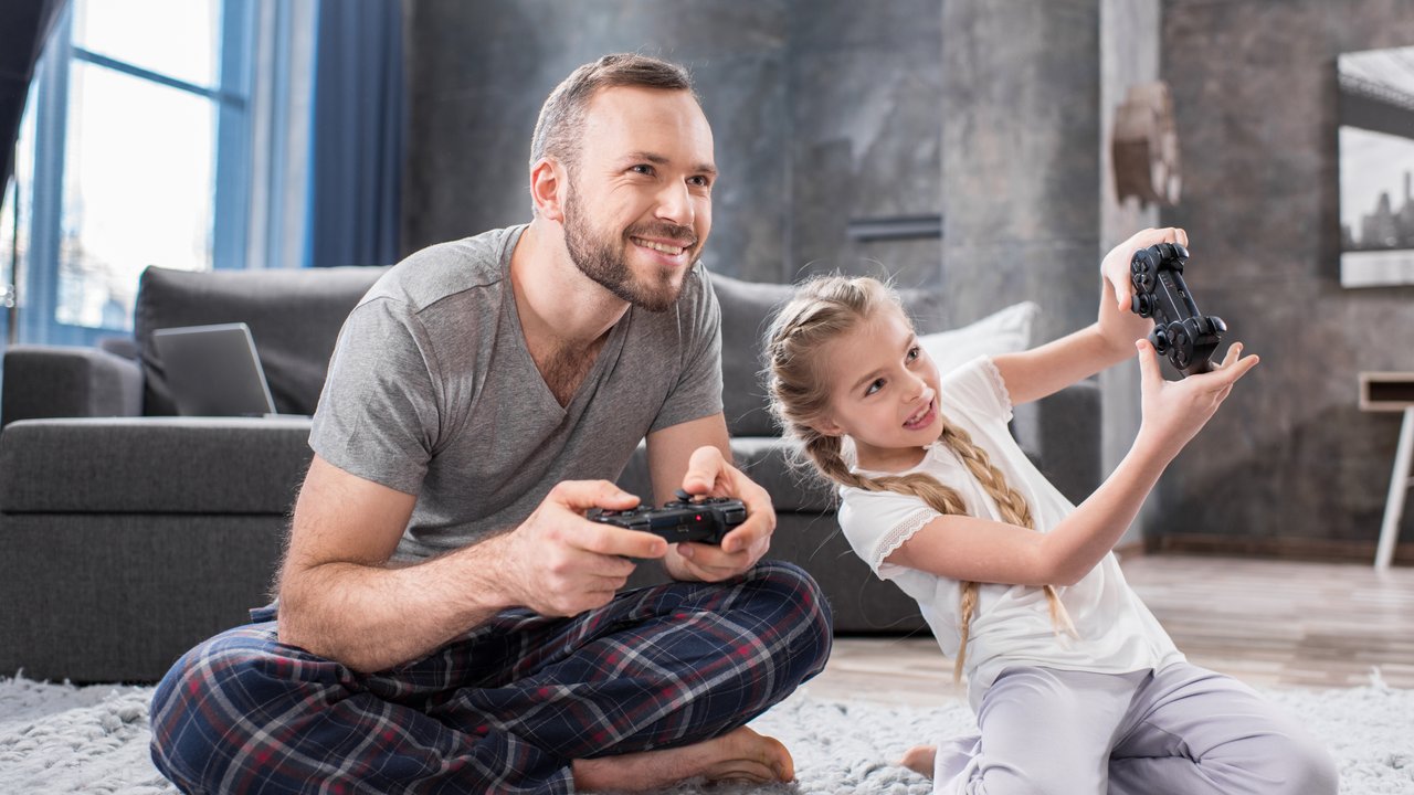 Happy father and daughter sitting on carpet and playing with joysticks