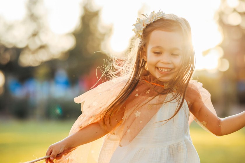 Cute little girl dressed in a fairy outfit using a twig as a magic wand.