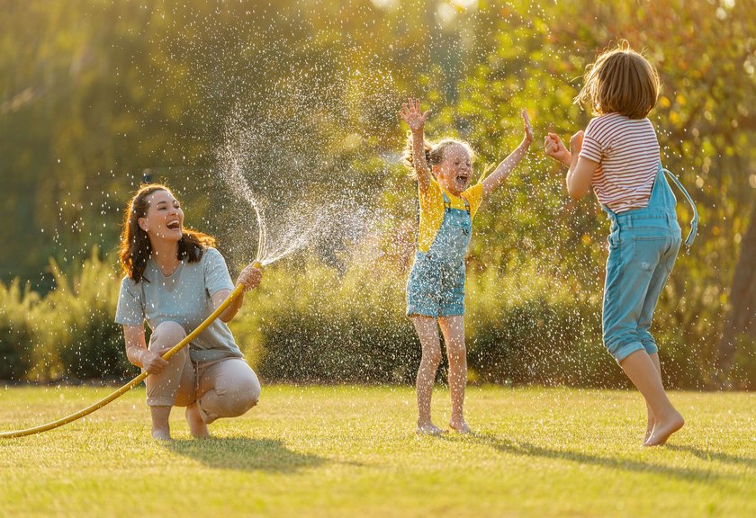 Mutter spritzt Kinder mit einem Gartenschlauch ab