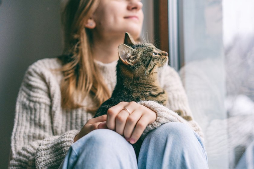 Mädchen sitzt mit Katze am Fenster